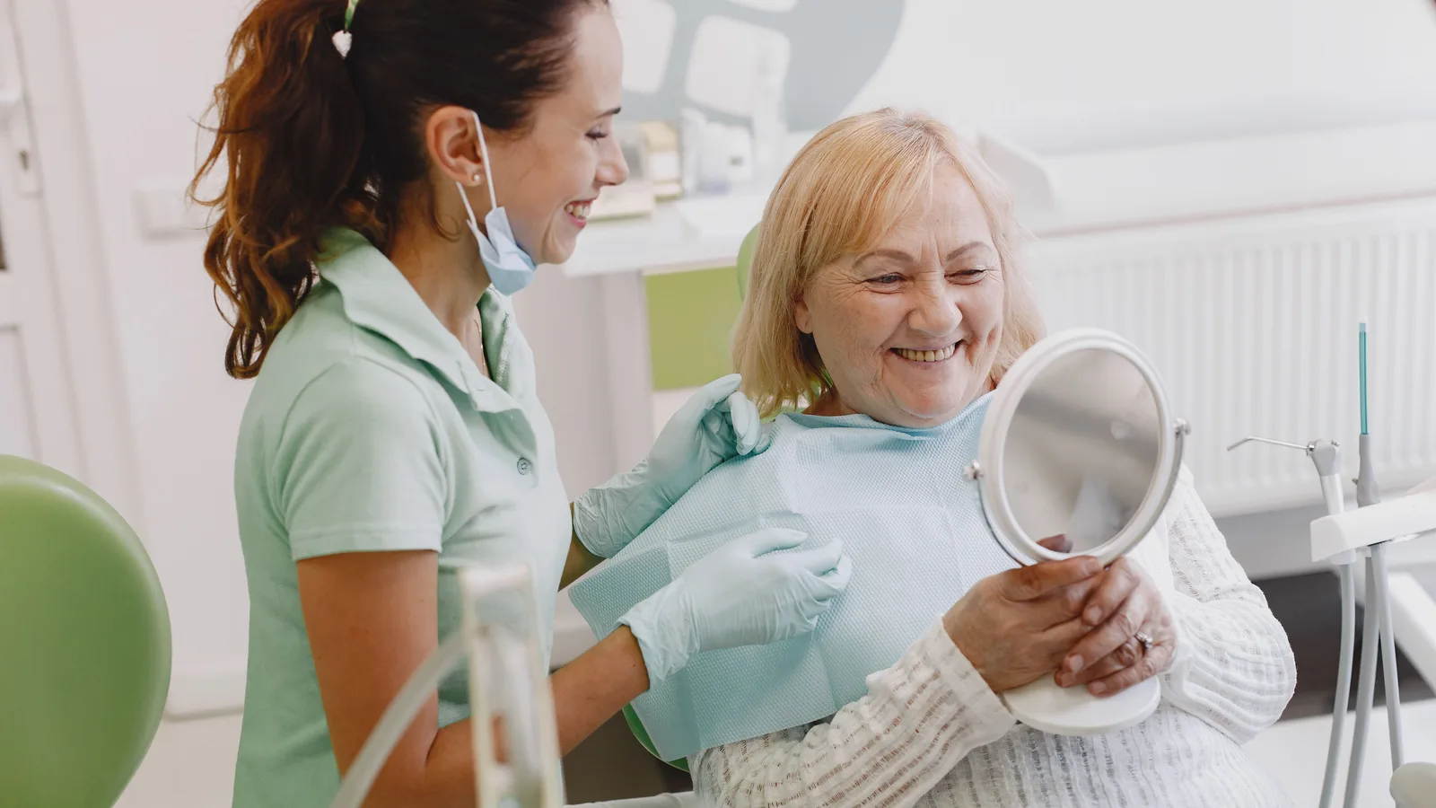 Hygienist and a smiling senior patient looking in a hand mirror